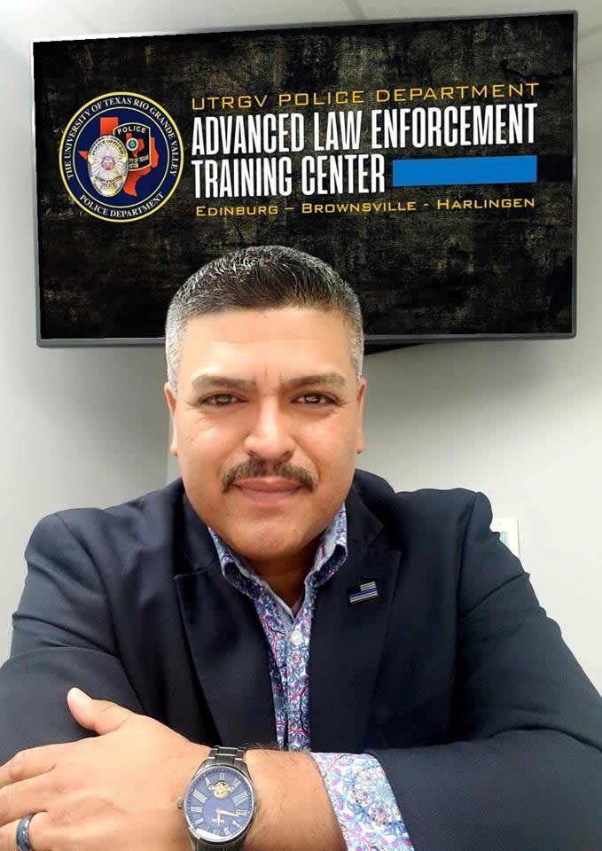 Office Zarzoza, arms crossed, stands in front of a sign that reads 'UTRGV Police Department Advance Law Enforcement Training Center'